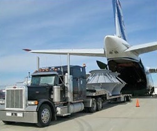 Flatbed truck with an oversized load beside a cargo aircraft